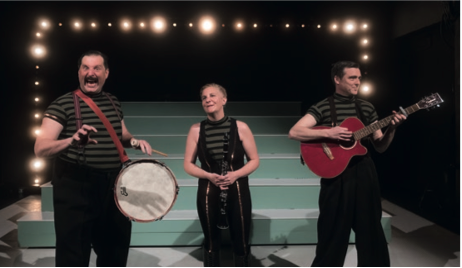 Sur une scène un comédien avec un tambourin, à ses cotéq une femme, puis un 3eme comédien, une guitare à la main. Des lampions derrière eux les encadrent.n